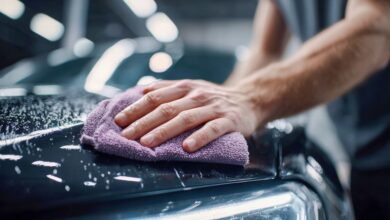 A man's hand wiping a wet car hood with a purple microfiber cloth, showcasing a car wash and detailing process.